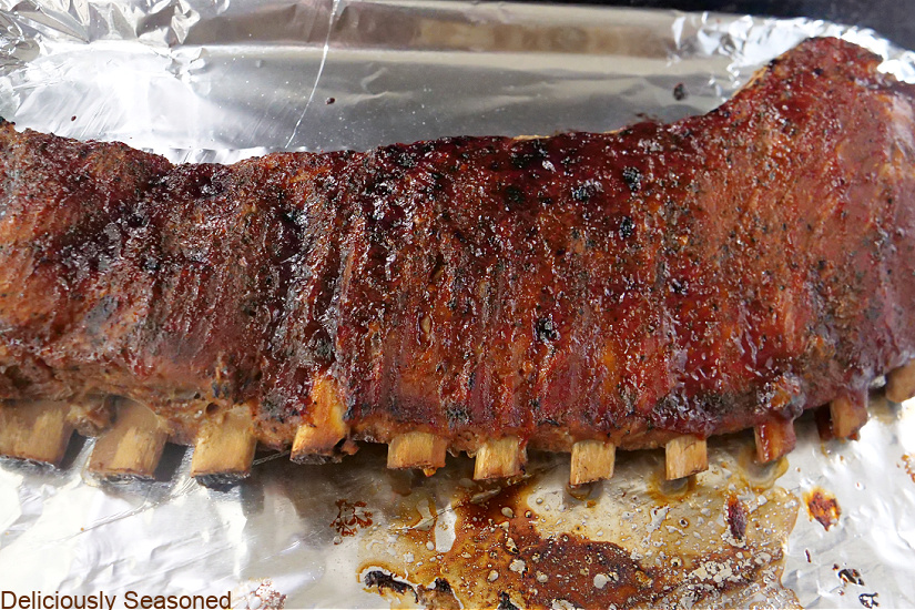 A baking sheet covered with aluminum foil with a rack of slow cooked ribs on it.