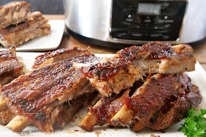 A white plate filled with crockpot pork ribs piled on it with one rib with a bite taken out.