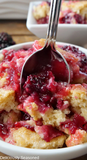 A close-up picture of blackberry cobbler in a white bowl with a spoon full of cobbler inside of the bowl.