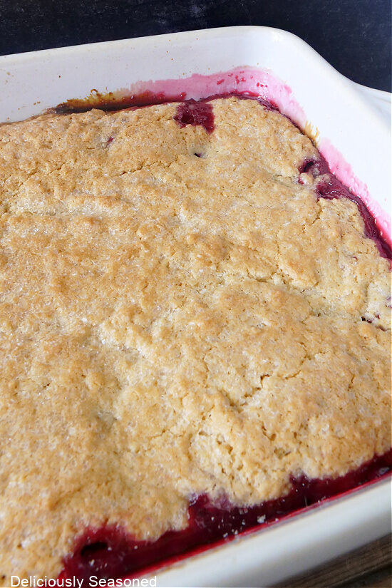 A close-up picture of blackberry cobbler inside of the baking dish, showing the buttery crumble topping and the blackberry filling oozing out of the sides.
