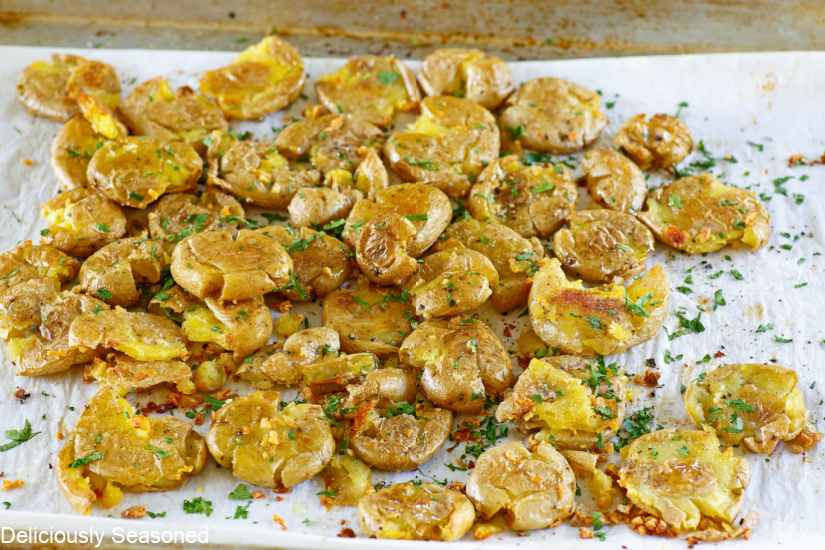 A baking sheet with parchment paper filled with smashed baby potatoes on it.