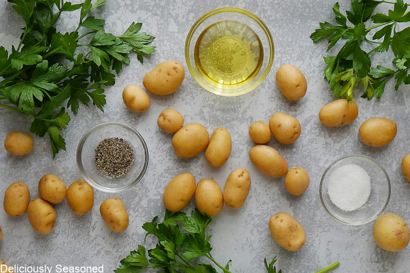 Baby potatoes with olive oil, salt, pepper, and parsley on a grey surface.