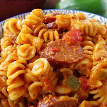 A bowl with blue trim loaded with rotini noodles, kielbasa, bell peppers, and vodka sauce.