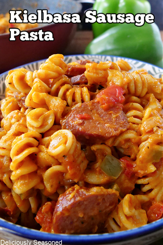 A bowl with blue trim loaded with rotini noodles, kielbasa, bell peppers, and vodka sauce.
