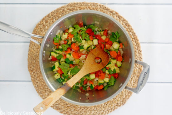 A large white surface with a round wicker placemat and a pan with diced vegetables in it. 
