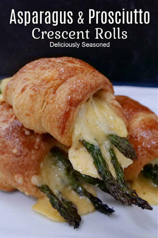 Three crescent rolls filled with prosciutto, asparagus, and gouda cheese, stacked up on a white plate.