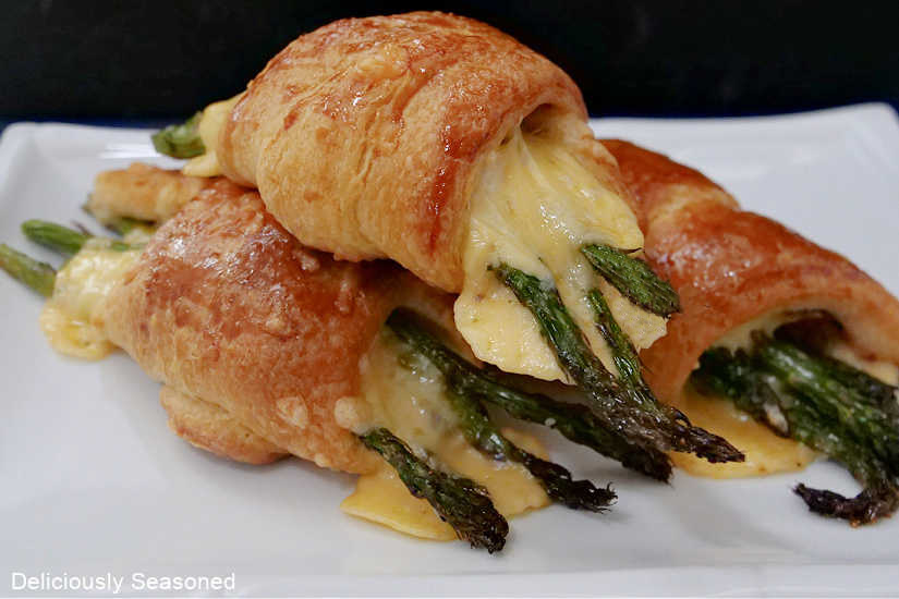 Crescent rolls filled with asparagus, melted smoked gouda, and prosciutto sitting on a white plate.
