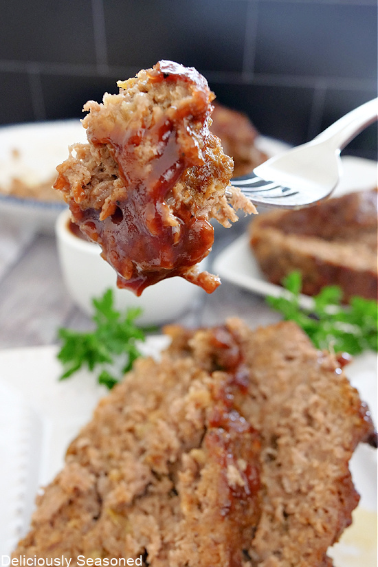 A bite of meatloaf on a fork with meatloaf on a plate in the background.