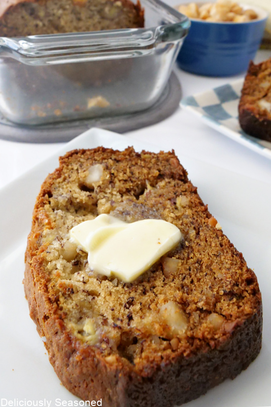 A slice of banana bread on a white plate with butter on it.