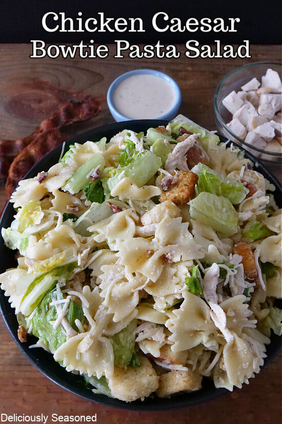 A black bowl filled with a serving of pasta Caesar salad.