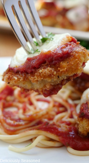A fork with a bite-size chicken parmesan piece held close to the camera lens.