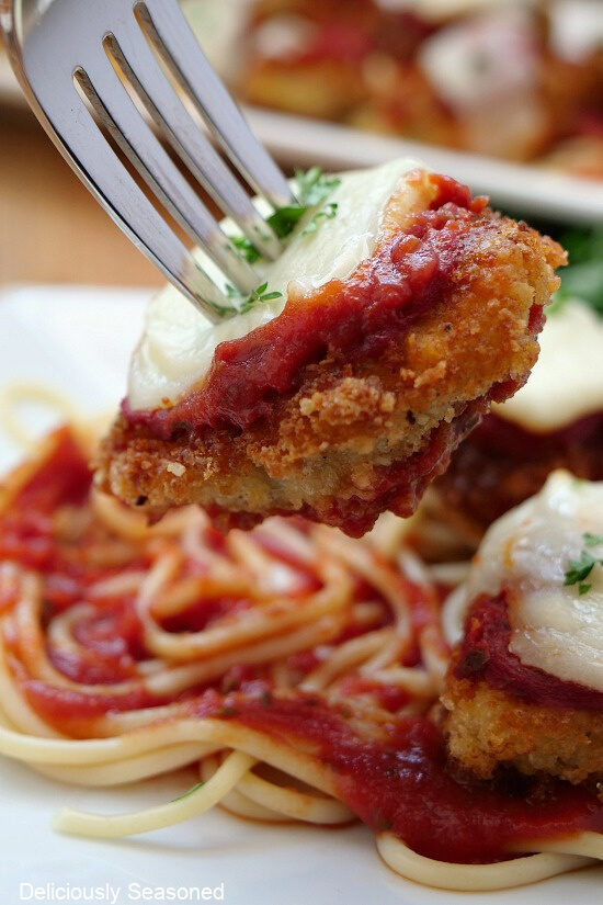 A fork with a bite-size chicken parmesan piece held close to the camera lens.
