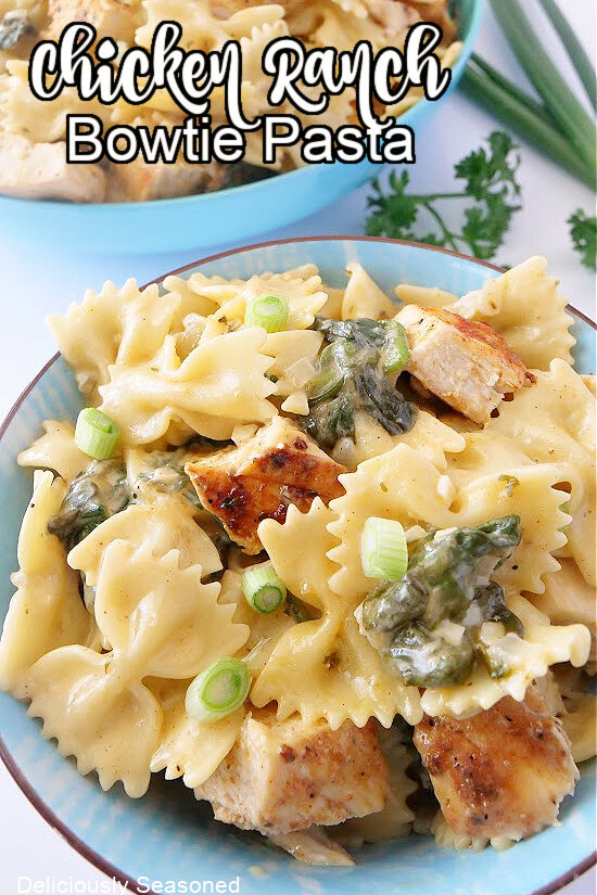Two blue bowls filled with bowtie pasta, chicken, spinach in a creamy sauce.