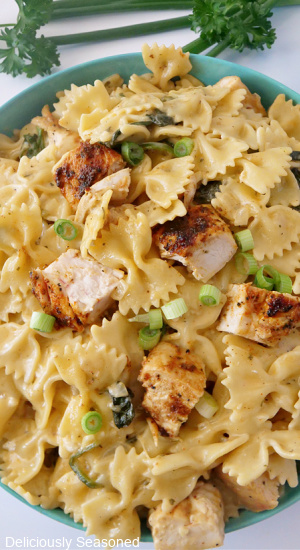 A close up view of a greenish blue bowl filled with pasta, chicken and spinach.