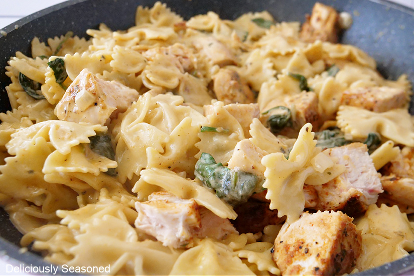 A pan filled with bowtie pasta, spinach and chicken in a creamy sauce.