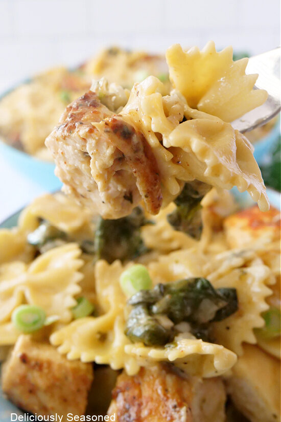 A close up photo of a bite of chicken and bowtie pasta on a fork.