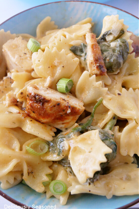 A close up photo of a serving of pasta, chicken and spinach in a light blue bowl.