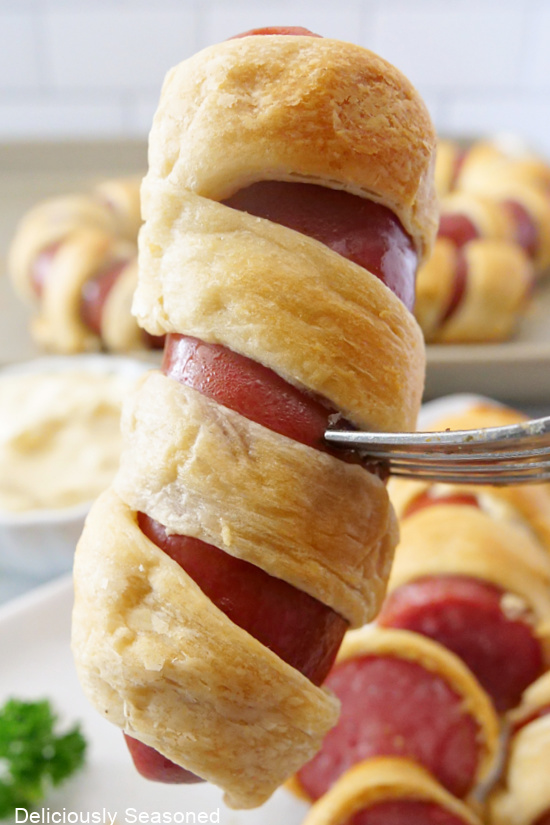 A piece of sausage being held up, showing the wrap of crescent roll around it.