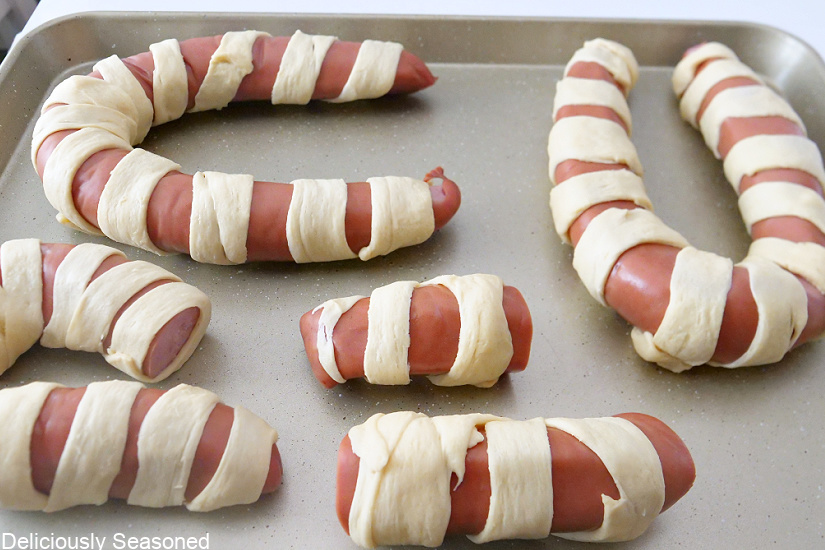 A cookie sheet with smoked sausage wrapped in crescent rolls that are unbaked.