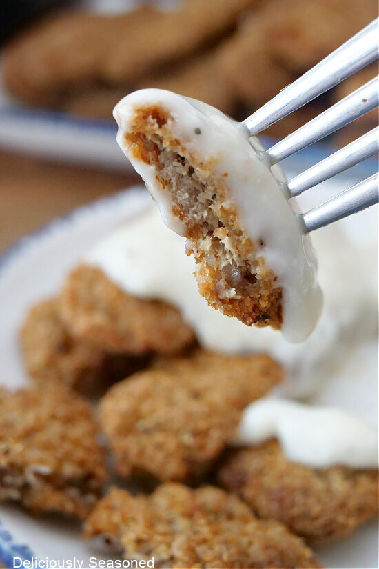 A close up photo of a fork with a bite of steak finger with country gravy on it.