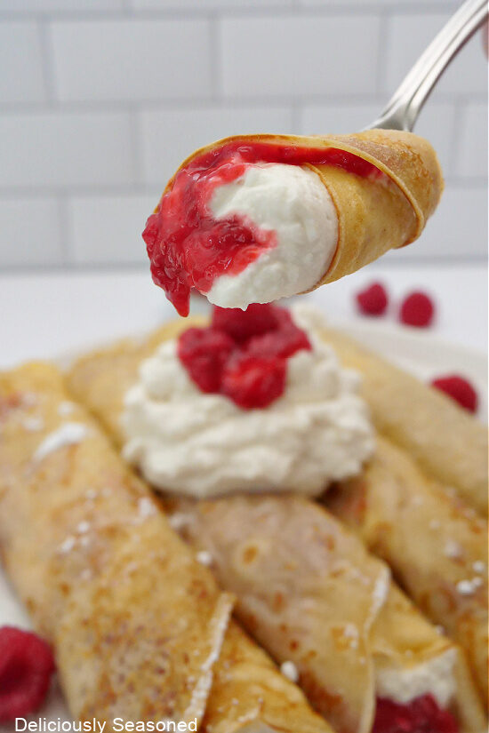 A bite of a raspberry crepe on a fork.