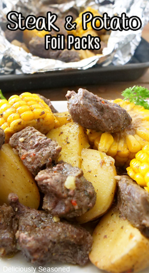 Bite-size pieces of steak, potatoes and sliced corn on the cob on a white plate.