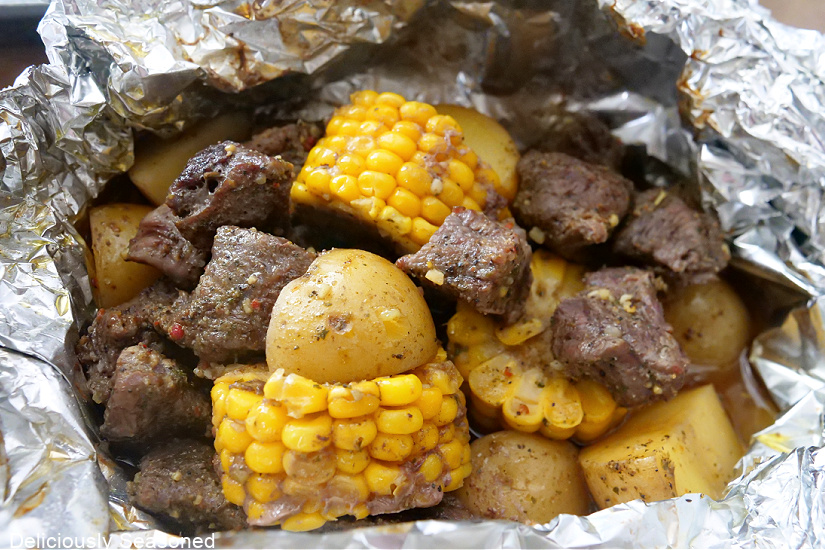 A foil pack after it has been oven-baked with steak, potatoes and corn.