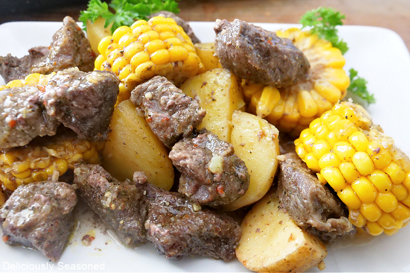 A white plate with bites of steak, potatoes and slices of corn on the cob.
