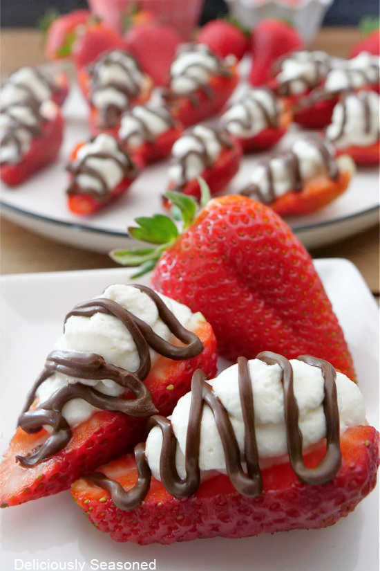 A close up photo of two strawberries topped with homemade whipped cream and a drizzle of chocolate.