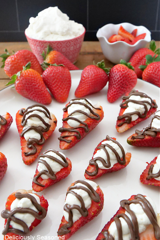 A large plate with whipped cream stuffed strawberries lined on it, all topped with chocolate.