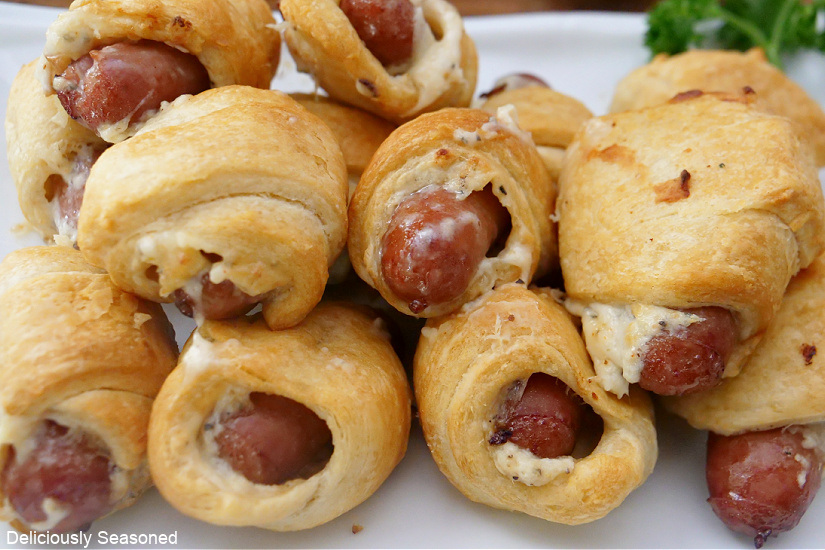 A horizontal pic of cheese pigs in a blanket stacked on a white plate.