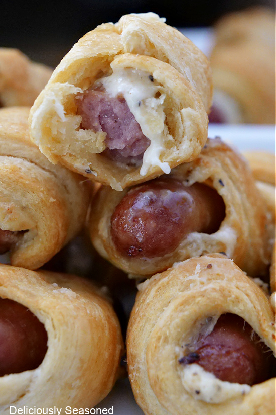 A close-up picture of cheesy crescent wrapped little smokies stacked on top of one another with a bite taken out of one.