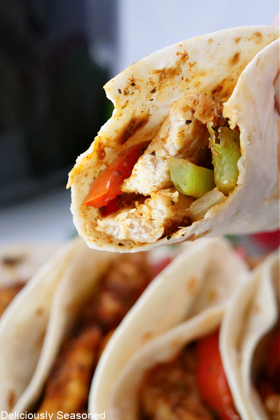 A close-up picture of chicken fajitas in a flour tortilla with a bite taken out of it.