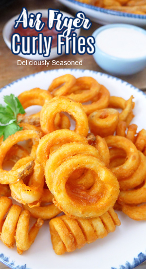 Crispy curly fries stacked up on a white plate with dipping sauce in the background. 