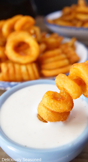 A curly fry being dipping in ranch dressing.