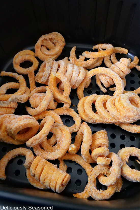 Frozen curly fries in an air fryer basket before being cooked.