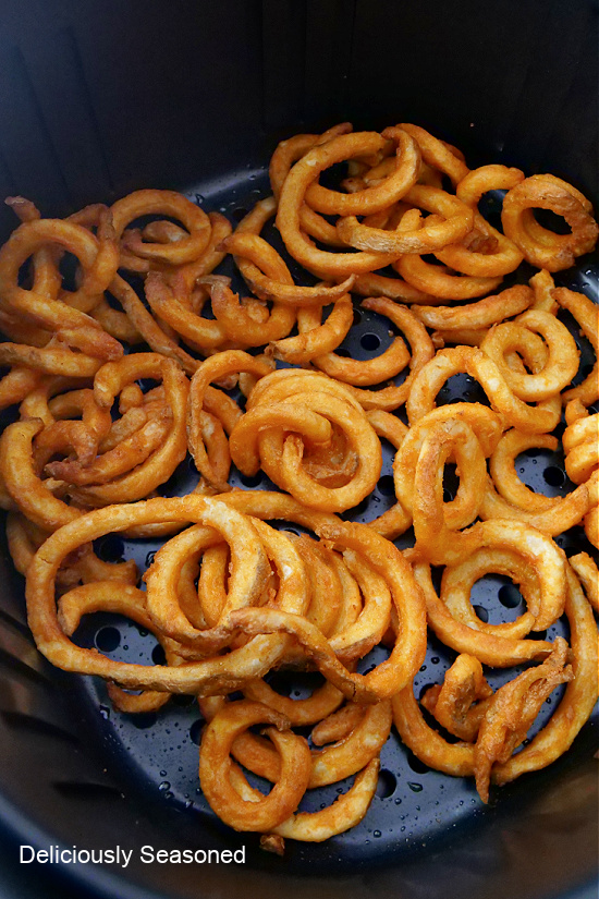 Crispy curly fries sitting in the air fryer basket.