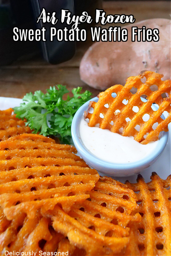 Waffle fries stacked up on a plate and a small blue bowl on the plate, filled with ranch with a waffle fry sitting in it.