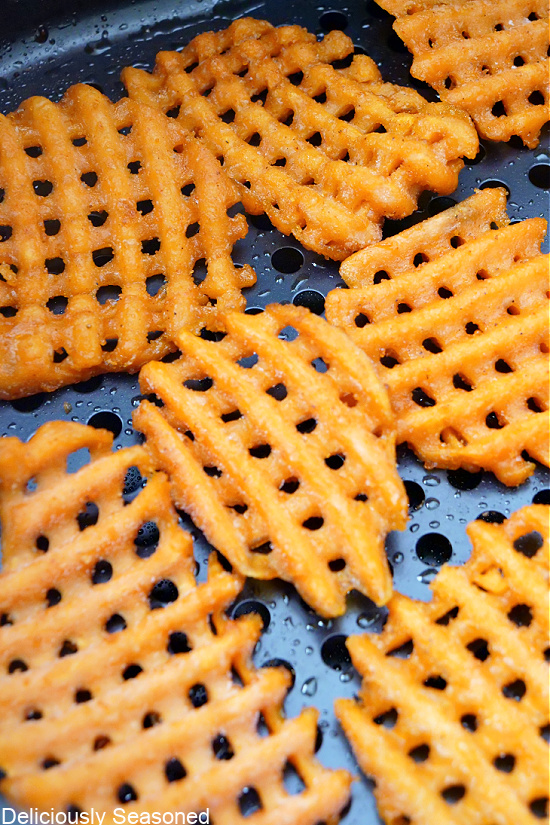Waffle fries lined in the bottom of an air fryer basket.