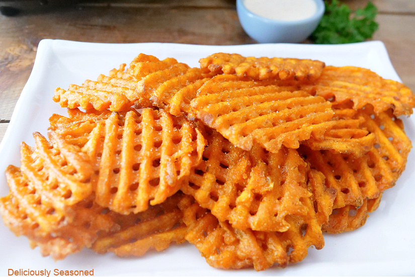 A horizontal photo of waffle fries stacked up on a white plate. 