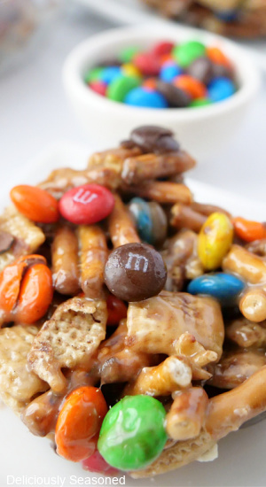 A close-up picture of a Chex Mix Bar on a white plate with a small bowl of M&Ms in the background.
