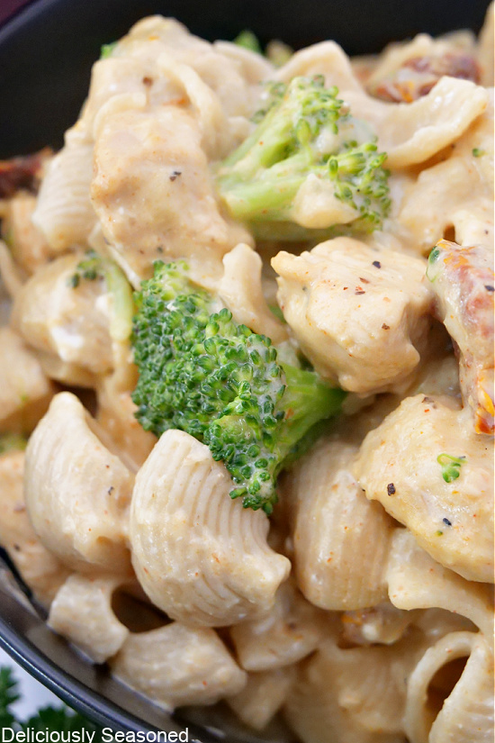 A close up photo of chicken and broccoli pasta in a black bowl.
