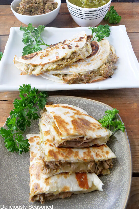 Chile Verde Quesadillas on a gray plate with a white plate in the background with more quesadillas on it.