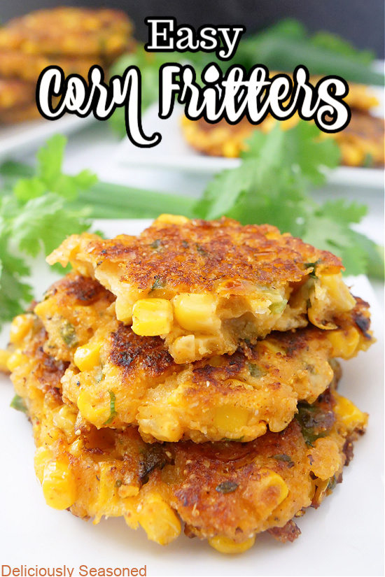 Three corn fritters stacked up on a white plate with more plates of fritters in the background.
