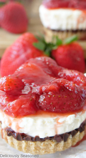 A cheesecake showing the four different layers in it topped with fresh strawberry sauce.