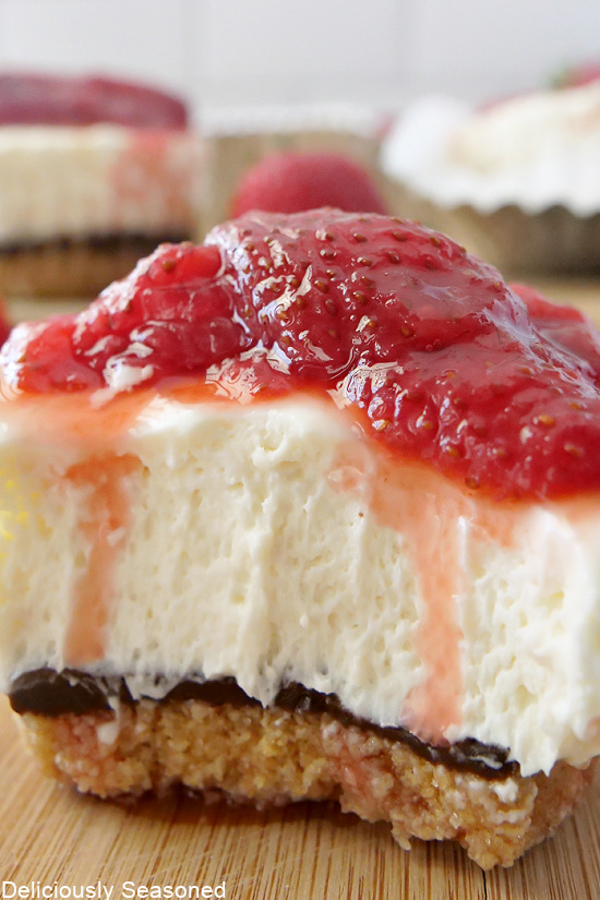 A close up pic of a mini cheesecake with a bite taken out of it, showing the layers of the dessert.