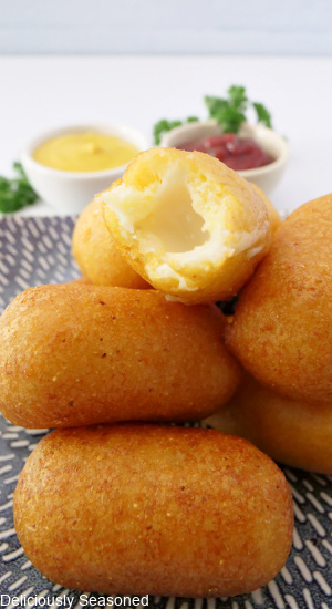 A plate filled with cheese bites with a cheese bite taken out of one, showing the cheesy inside.