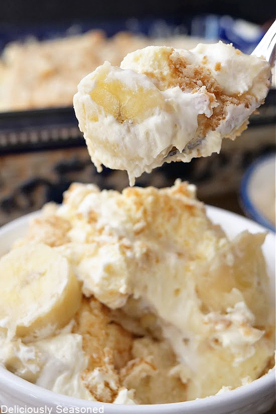 A white bowl filled with banana pudding and a spoonful of pudding being held up.