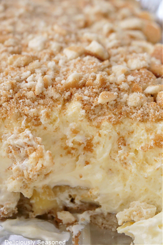 A close up photo of a casserole dish filled with banana pudding, topped with crushed vanilla wafers.