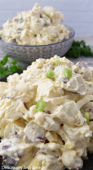 A close-up picture of red skinned potato salad with another bowl full of potato salad in the background.